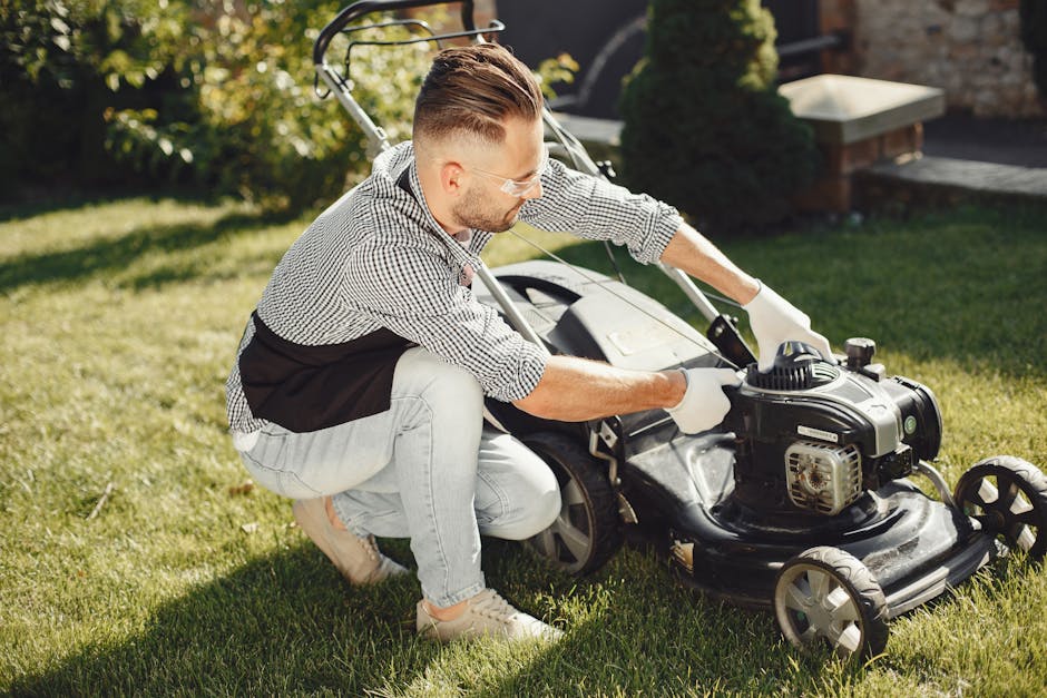 A silver metal wheelbarrow filled with a variety of garden waste, including wilted flowers, dried leaves, and plant cuttings, resting on a lush green lawn. The wheelbarrow has black handles and a stur